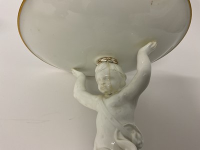 Lot 6 - Set of four 19th century white glazed tazzas, each in the form of a circular dish being held aloft by a putto, the bases decorated in gilt, 24.5cm high