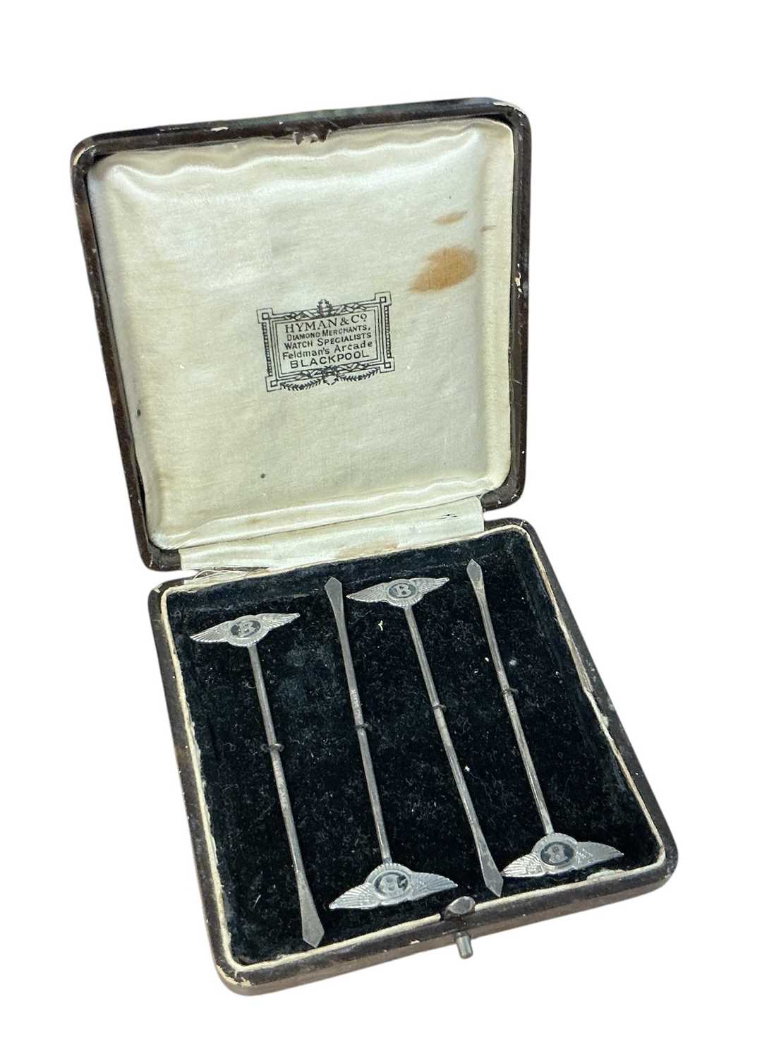 Lot 93 - Set of four 1930s silver cocktail sticks, each mounted with a Bentley winged B logo and stamped 'Sterling Silver', in a fitted case, each 8.5cm in overall length