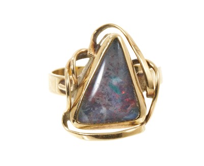 Lot 418 - Black opal ring with a triangular cabochon opal (possibly a doublet) in gold closed-back setting with gold scrolls on plain shank