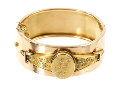 Lot Victorian yellow metal hinged cuff bangle with stylised buckle design, ivy leaf decoration and a glazed locket compartment to the inside