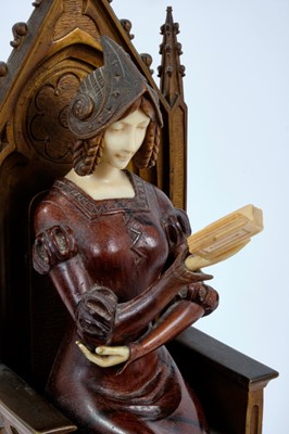 Lot 823 - In the manner of Jean Dampt (1854 - 1945): a late 19th century French Gothic Revival bronze, ivory and rosewood figure of a young woman dressed in medieval costume, seated on a throne reading a boo...